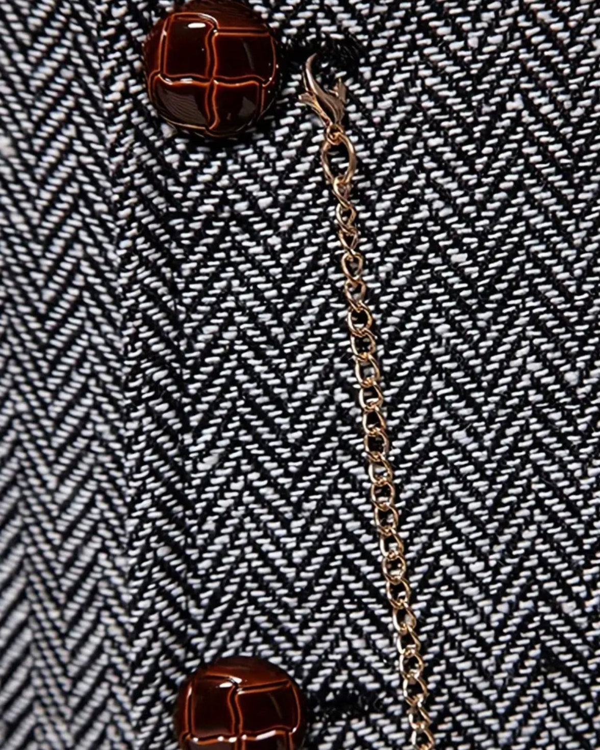 Nahaufnahme des Fischgrat-Tweeds der Lancaster Weste mit Knopf und goldener Kette